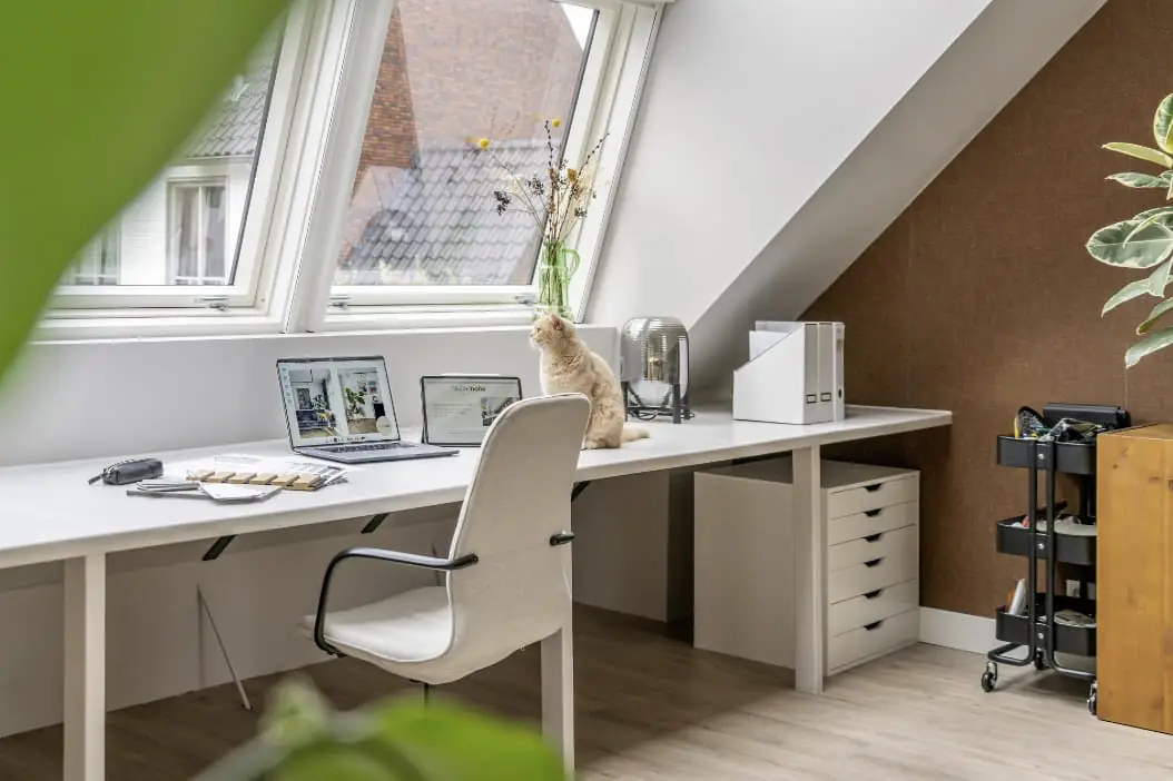 De dakserre op de zolder werkkamer is wit gecoat en er is een werkplek met wit bureau en een witte bureaustoel gemaakt.